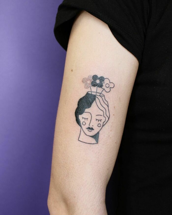 Minimalist flower tattoo on arm, featuring a woman's face and flowers in black and white.