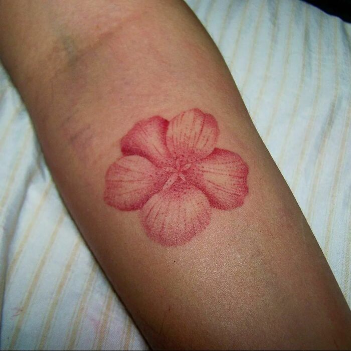 Red flower tattoo on arm, showcasing elegance and beauty with delicate petal details.
