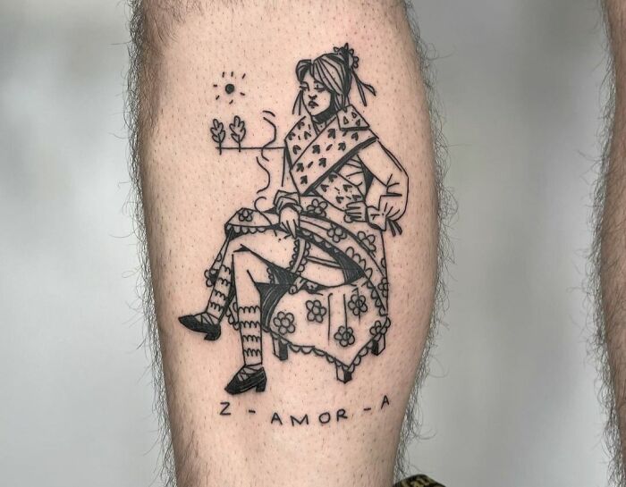 Self-love tattoo featuring a seated woman in detailed attire with the text "Z - AMOR - A" on a person's leg.