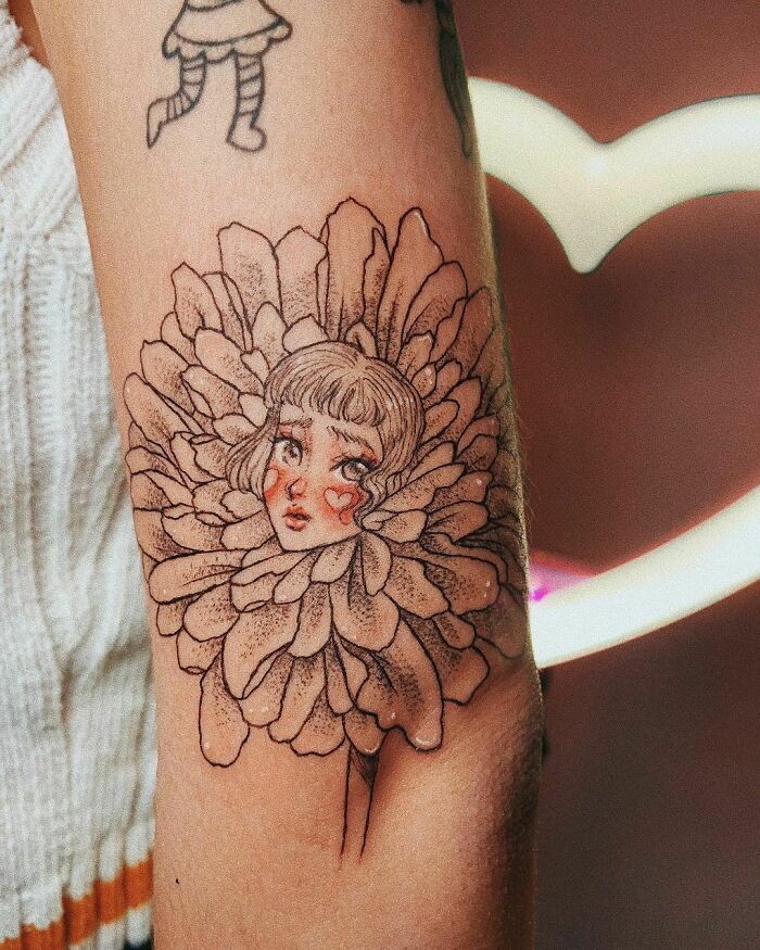 Elegant flower tattoo featuring a woman's face surrounded by petals on an arm.