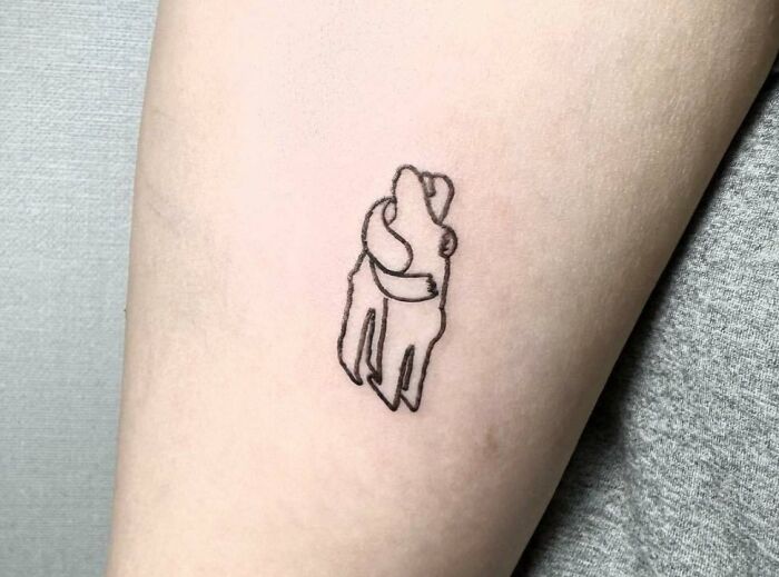 Minimalist self-love tattoo of two hugging figures on forearm.