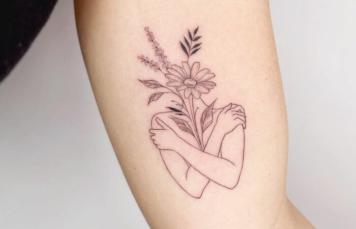Woman hugging herself with flowers tattoo 