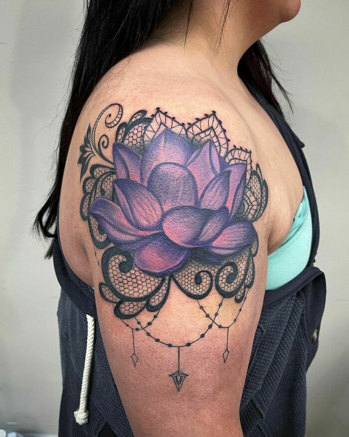 Purple flower tattoo with lace details on upper arm, showcasing elegance and beauty.