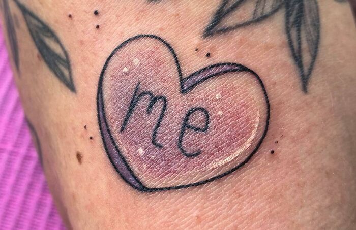 Heart-shaped self-love tattoo with the word 'me' inside, featuring pink shading and black outlines.