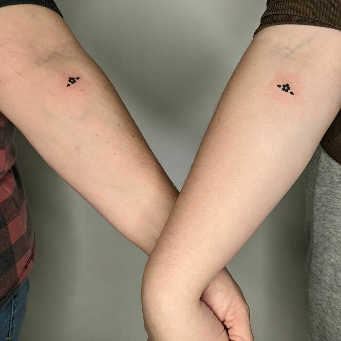 Two forearms with small flower tattoos, showcasing elegant tattoo designs.