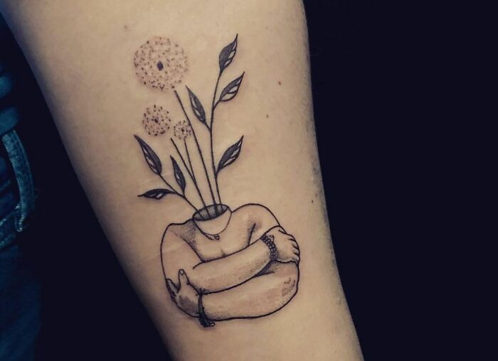 Person hugging himself with flowers head arm tattoo