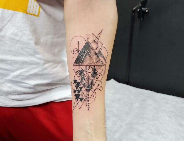 Geometric tattoo with mountains and trees on an arm, featuring intricate patterns and lines.