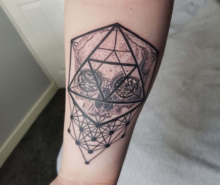 Geometric tattoo featuring a skull with intricate patterns and lines on a forearm.