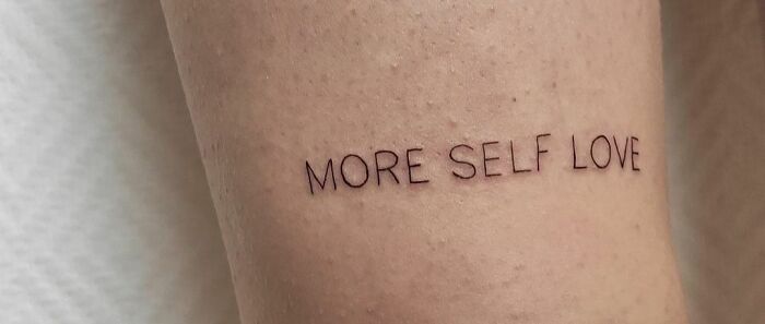 Self-love tattoo with the words "MORE SELF LOVE" on skin.