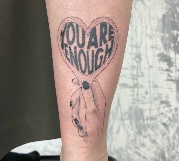 Self-love tattoo of a hand holding a heart with "YOU ARE ENOUGH" written inside, symbolizing empowerment and inspiration.