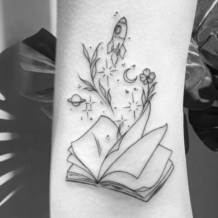 Book with flower and spaceship with stars and planets arm tattoo