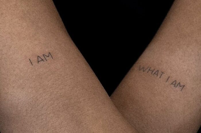 Self-love tattoo on arms reading "I AM WHAT I AM," emphasizing empowerment and personal affirmation.