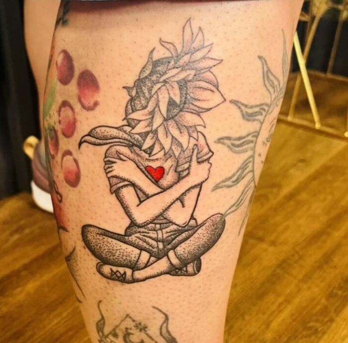 Person huggin himself with flower head leg tattoo