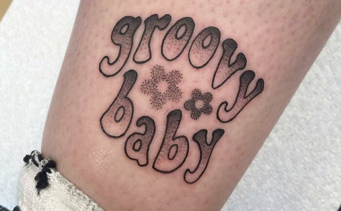 Self-love tattoo with "groovy baby" text on skin, featuring floral details.