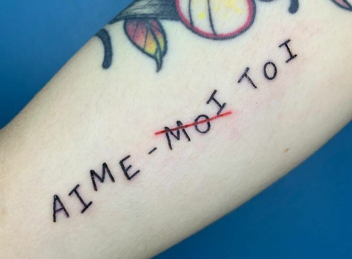 Tattoo with French text "AIME-MOI TOI" symbolizing self-love and empowerment, with floral accents.