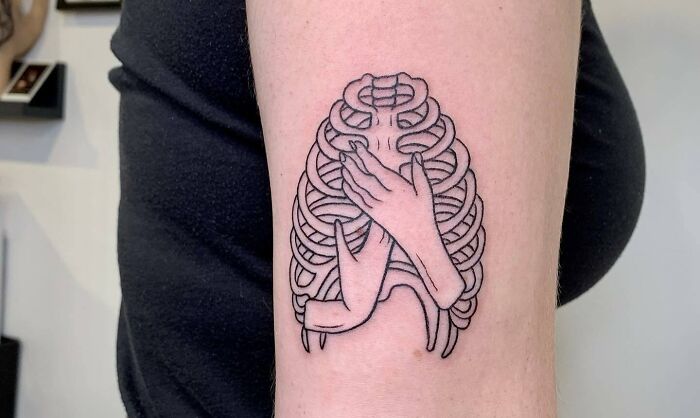 Tattoo of hands hugging a ribcage symbolizes self-love on a person's arm.