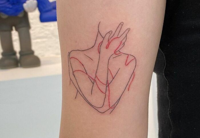 Self-love tattoo of an abstract line art design on an arm, featuring intertwined red and black lines.