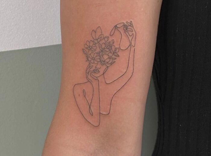 Line art tattoo of a figure holding flowers, symbolizing self-love and empowerment.