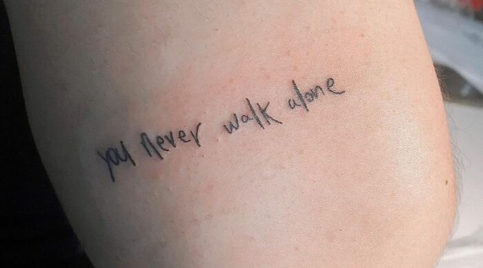 Self-love tattoo text "you never walk alone" on skin.