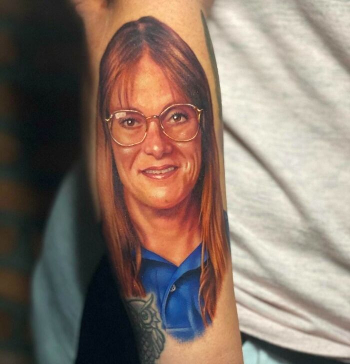 Realistic tattoo of a woman with glasses and long hair on an arm, showcasing intricate detail and vibrant colors.