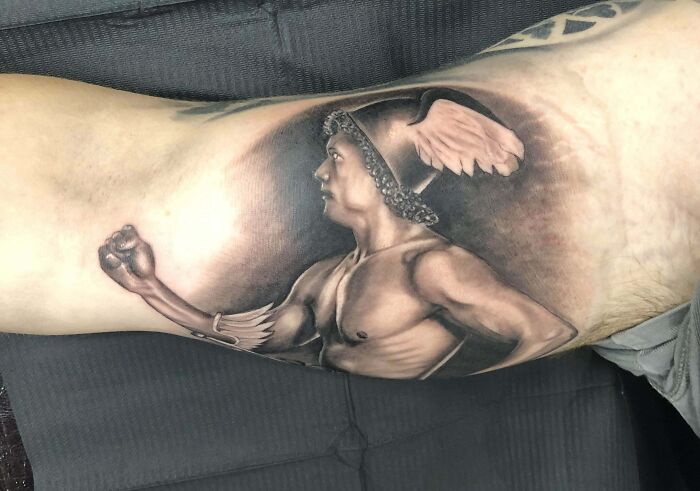 Realistic tattoo of a Greco-Roman warrior with detailed helmet and plume, inked on an upper arm, showcasing artistic precision.