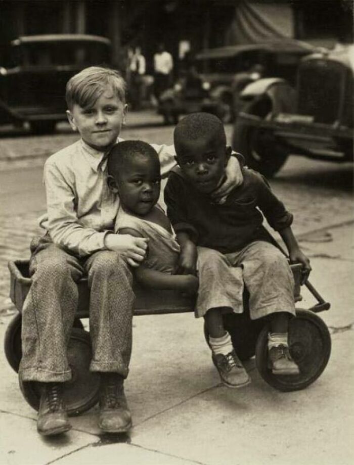Tres niños sentados en un carrito en una calle de un barrio de Pittsburgh, 1920-1930