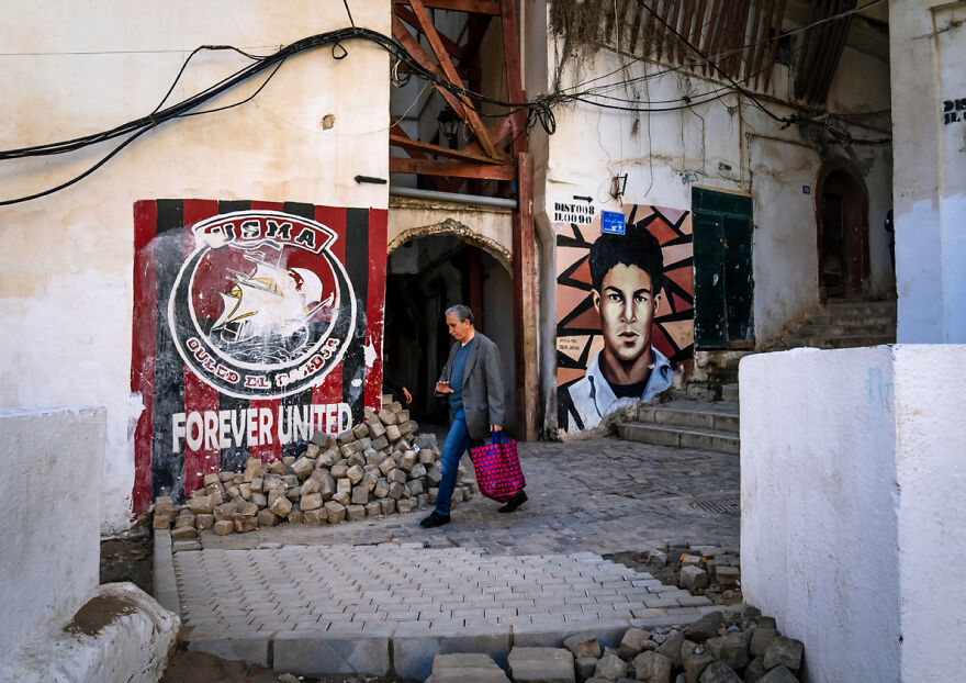 Man Passing Near Murals Of Football And Revolution In The Casbash, North Africa, Algiers, Algeria