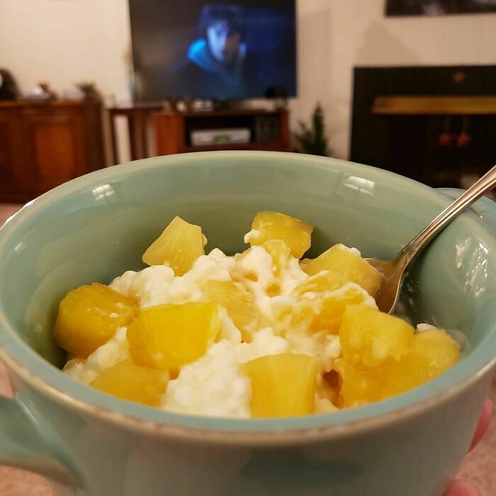 Person eating cottage cheese and pineapple while watching TV