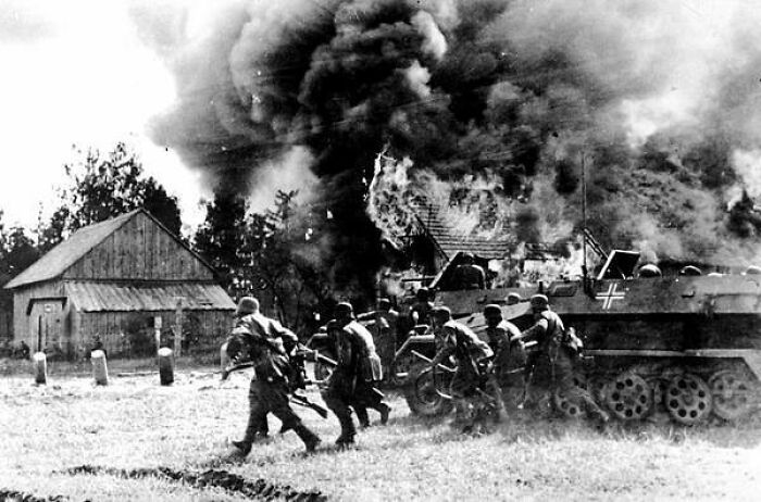 German Soldiers Supported By Armored Personnel Carriers, Move Into A Burning Russian Village At An Unknown Location During The German Invasion Of The Soviet Union On June 26, 1941