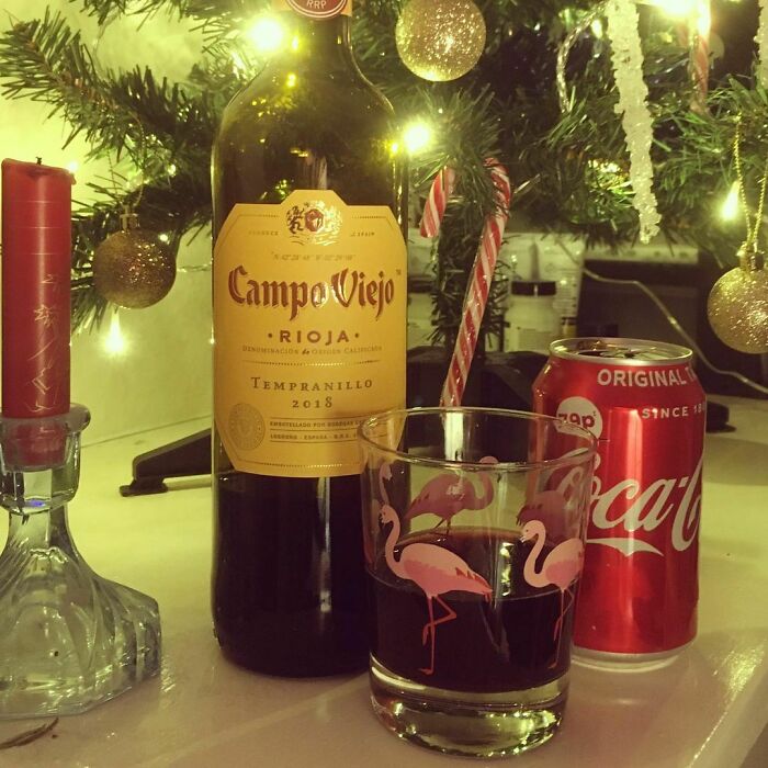 Bottle of wine and glass of Coca-Cola near Christmas tree