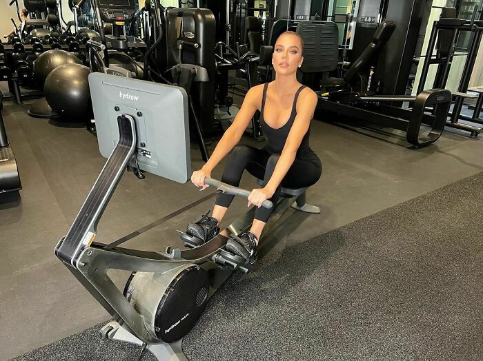 Celebrity in gym using a rowing machine, wearing sporty clothes.