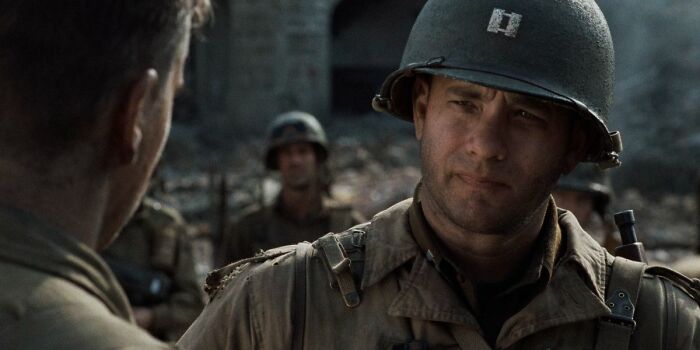 Tom Hanks in a World War II scene wearing a military helmet and uniform, featured among highest-paid actors.