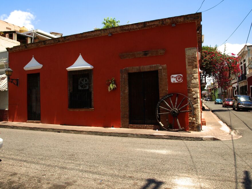 A Red, Colonial Building In The Colonial City With A Wooden Wheel Against Its Wall