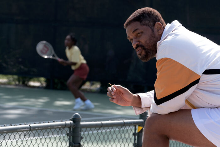 Actor coaching tennis player on court during a scene featuring one of the highest-paid actors of all time.