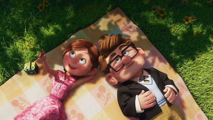 Ellie and Carl smiling and laying on a blanket outside 