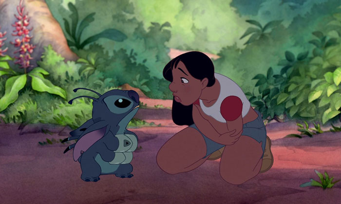 A young girl kneels in a jungle, holding a paddle, while talking to a small blue creature.