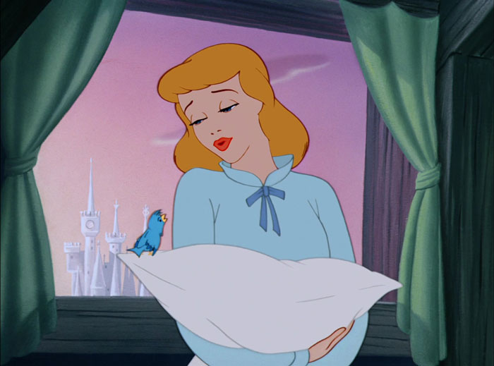 Cinderella holding a pillow and looking at a small blue bird in the background of a window