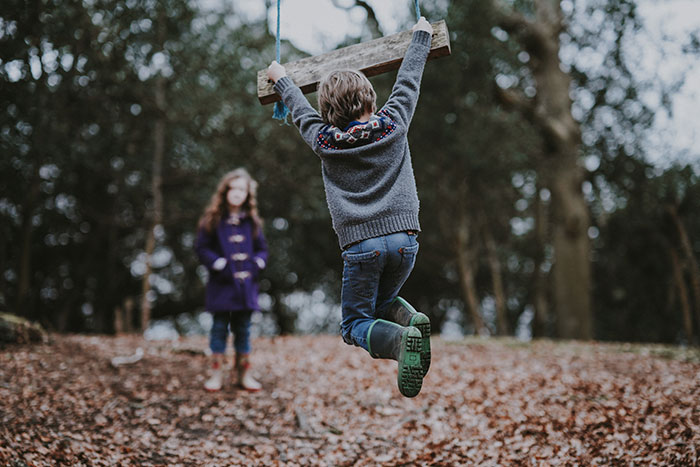 Children playing on tree swing in woods