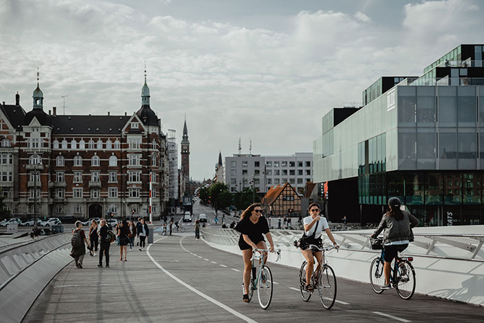 people biking and other people walking on pathway near buildings under white and blue sky