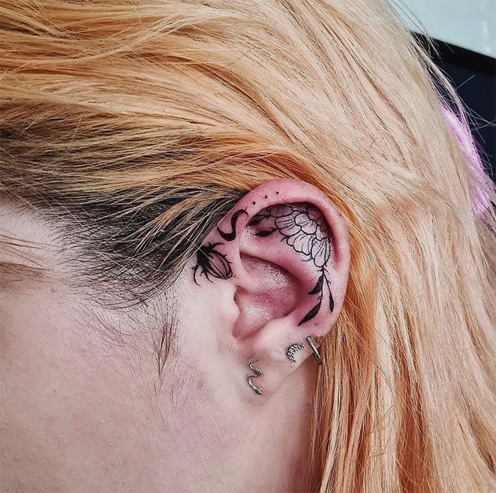 Floral ear tattoo design with intricate black ink detailing on a person's ear.