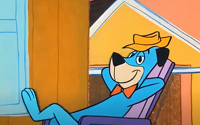 A famous cartoon dog in a hat, lounging on a chair with a relaxed expression.