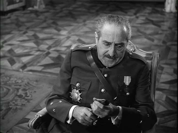 Adolphe Menjou sitting in a chair and holding something 