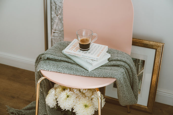 Pink chair with books, a glass mug, and a cozy blanket for home organization, accented with flowers underneath.