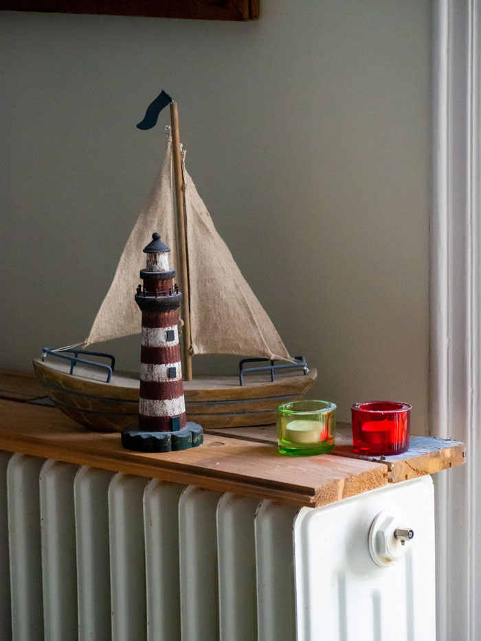 Model ship and lighthouse decor on a wooden radiator cover, illustrating creative home organization ideas.
