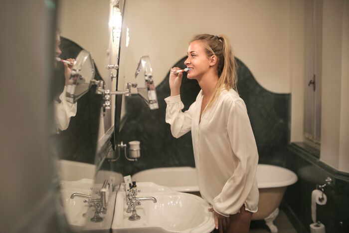Woman Brushing Teeth In Front Of Mirror