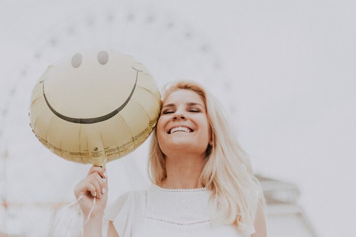 Woman Smiling Holding A Smiley Face Balloon 