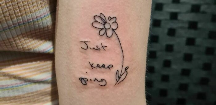 Self-love tattoo with a flower and the words "Just keep going" on an arm.
