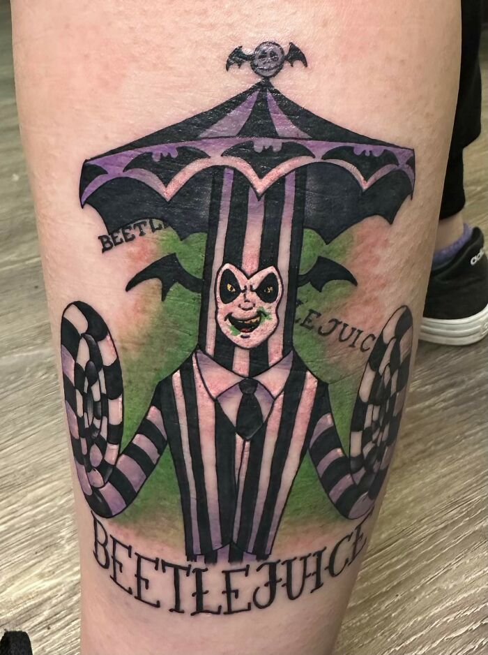 Beetlejuice-inspired tattoo with striped suit and umbrella design on leg.
