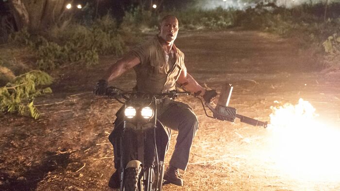 Actor riding a motorcycle at night with a flamethrower, featured among the highest-paid actors in the industry.