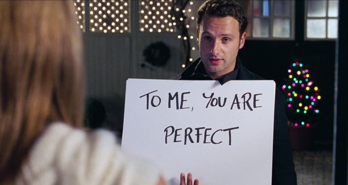 A man holding a poster to a woman "To me you are perfect"